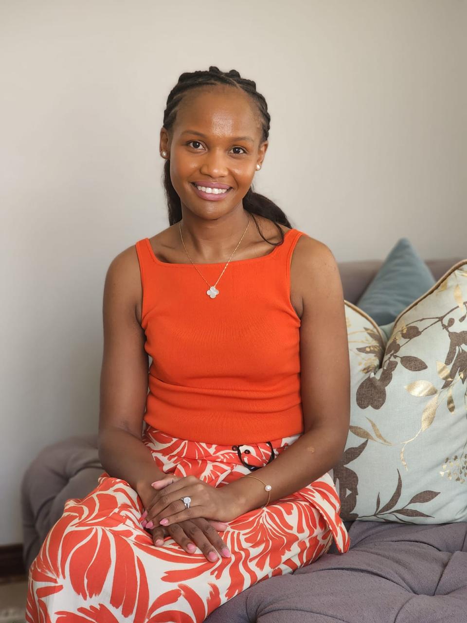 Sheila, founder, smiling warmly on a sofa in an orange top and floral skirt